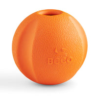 Ein Beco Fetch Ball aus Naturkautschuk in der Hand eines Hundebesitzers, der ihn für ein Wurfspiel im Freien vorbereitet. Der Ball ist elastisch, robust und mit einem angenehmen Vanilleduft versehen, um den Hund zum Apportieren zu motivieren.